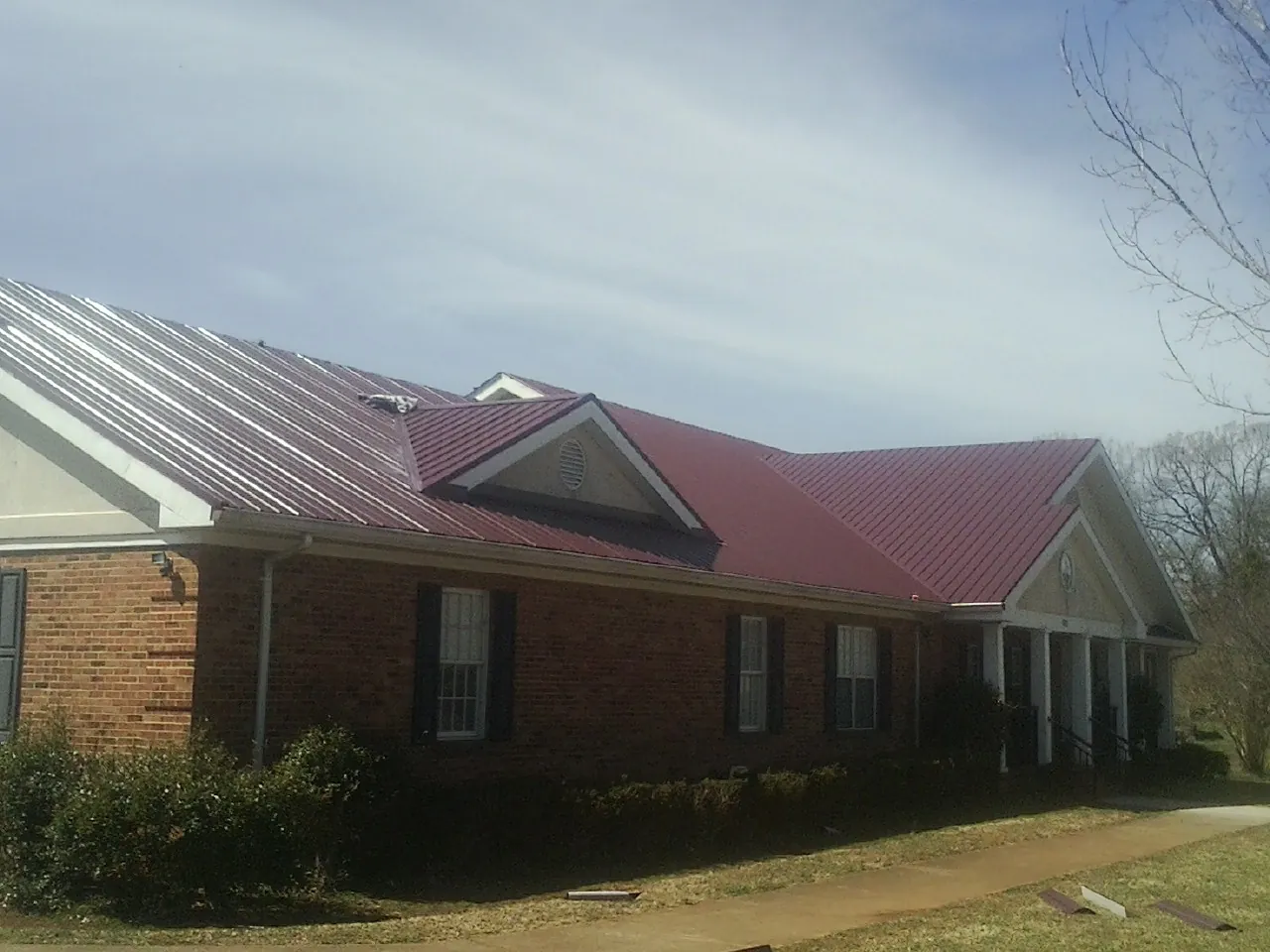 Red metal roof with gabled entries on a long brick building, from a Hail Damage Roof Repair job in Phoenicia