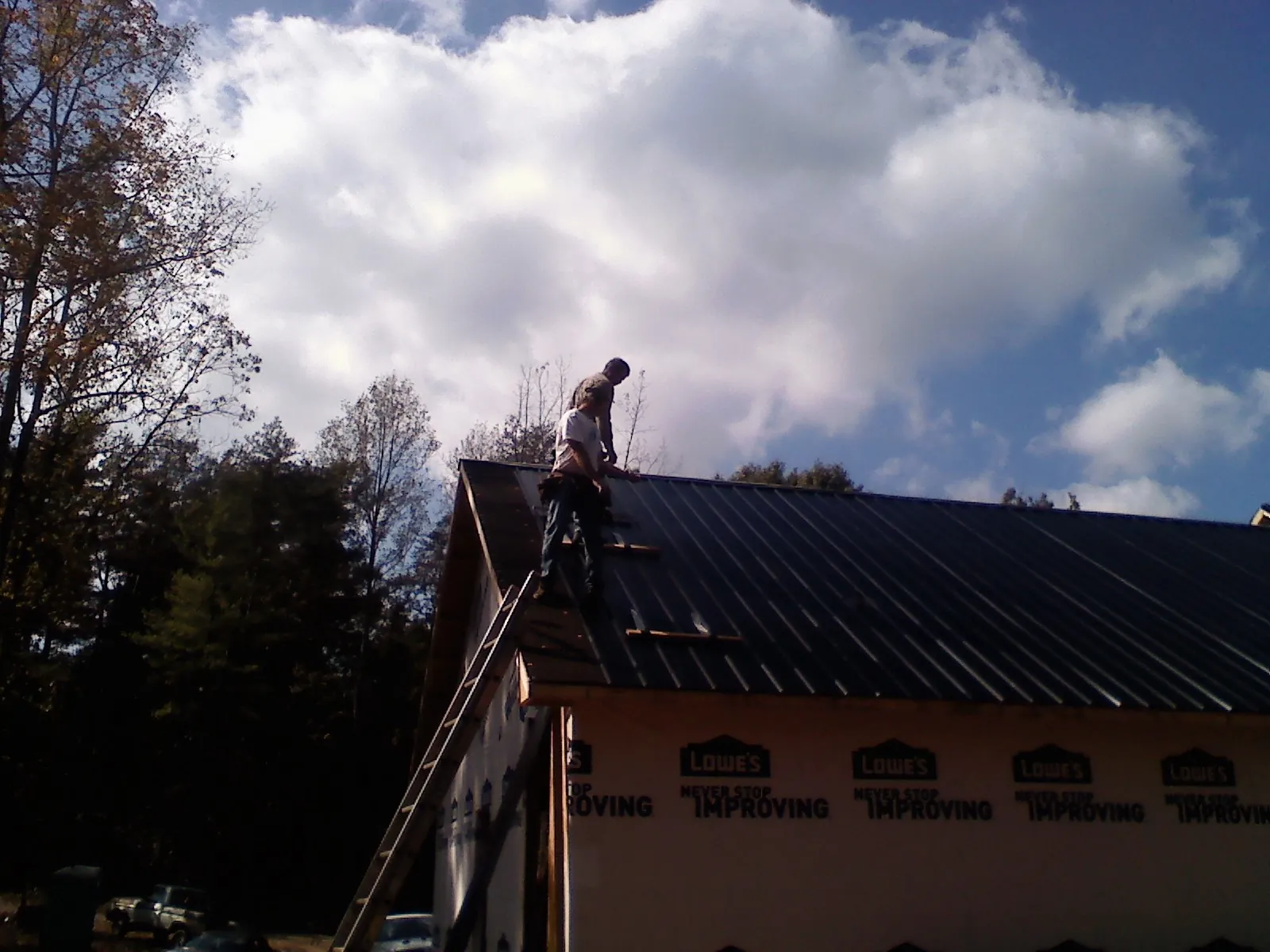 Roofer fastening dark metal panels high against a cloudy sky, from a Roof Inspection job in Phoenicia