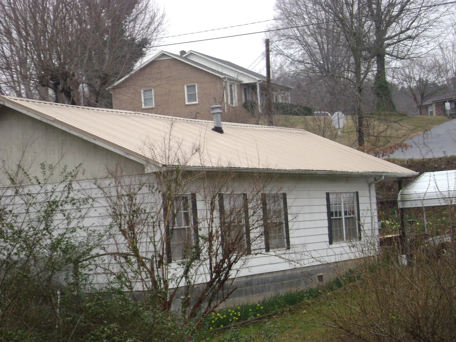 Tan metal roof on a white sided house set into a hillside — Commercial Roofing by Roofing Brothers in Phoenicia